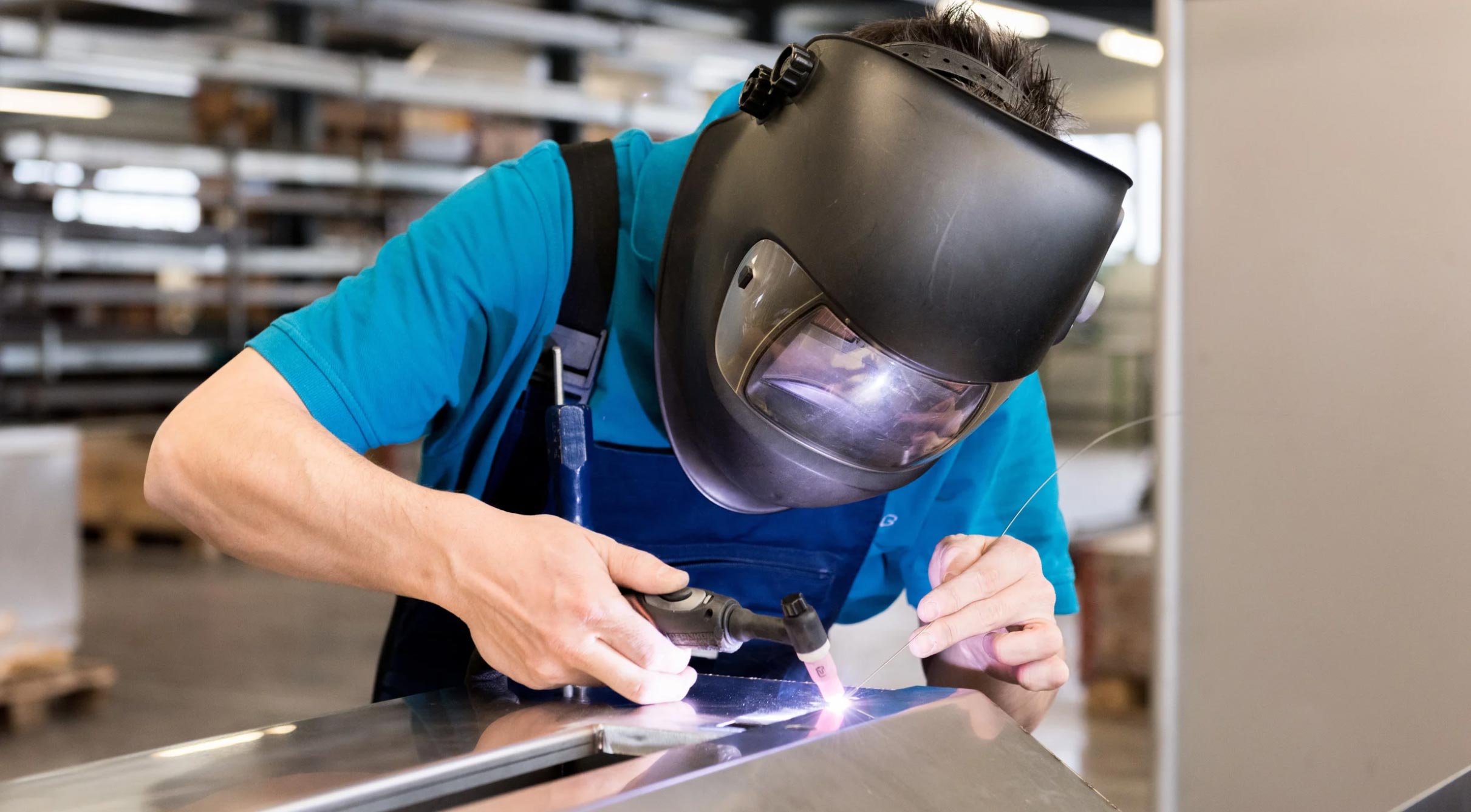 welding-6-img Person wearing a welding helmet welding metal in a workshop or industrial setting.