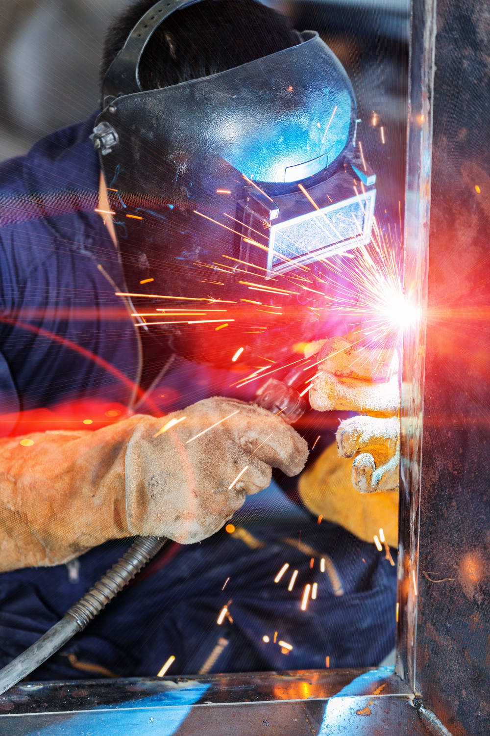 A person performing mobile welding on metal while wearing protective gloves and a dark face shield, with bright sparks flying.