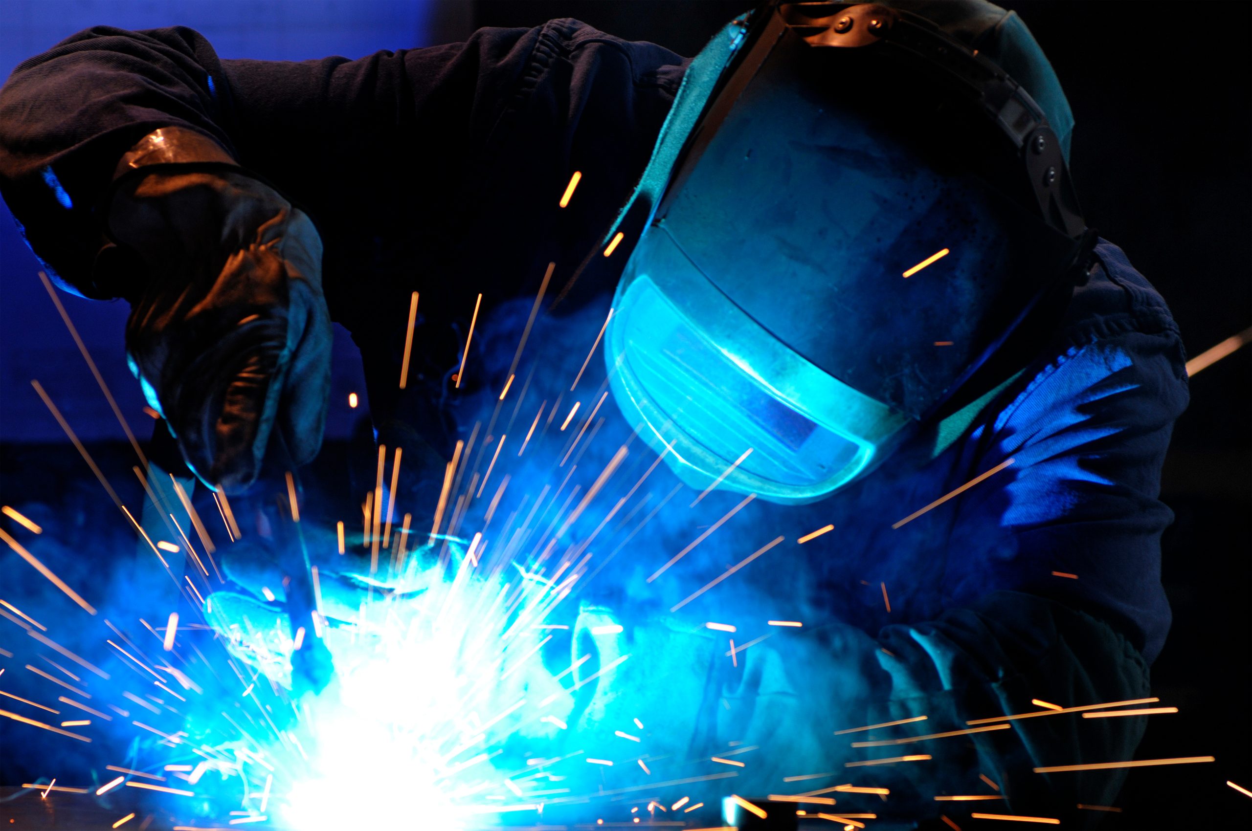 Person welding metal, wearing protective gloves and a helmet, with bright sparks and blue light—perfect for those tackling challenging welding projects.