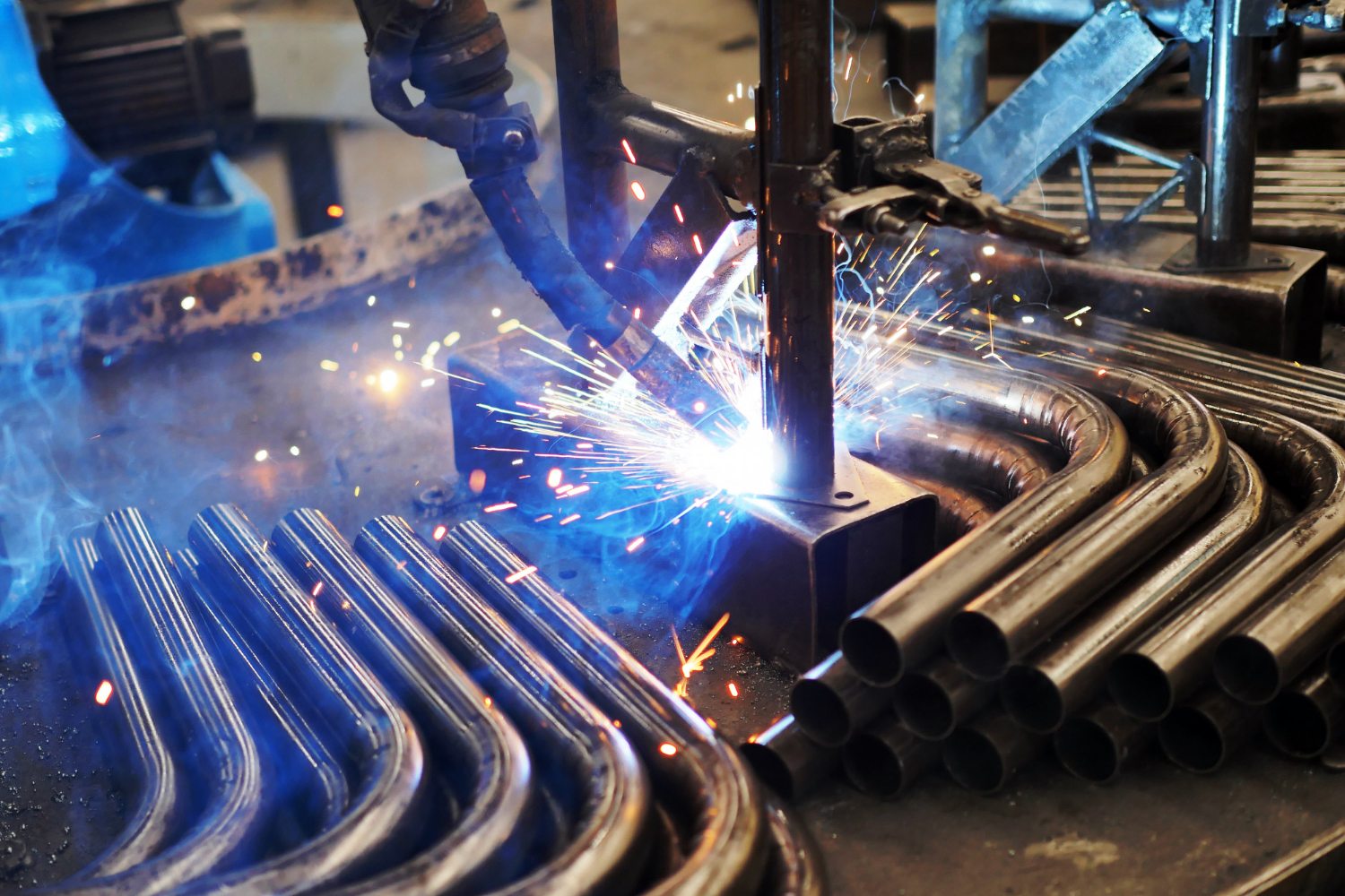 Close-up of a welding machine joining metal pipes, with bright sparks and curved pipes surrounding the work area—an impressive display of precision metal fabrication.