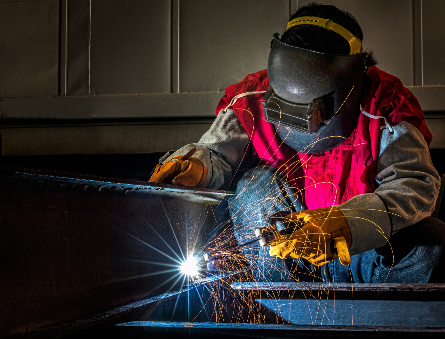 A welder in protective gear uses a torch, creating bright sparks and light while performing mobile welding on metal.
