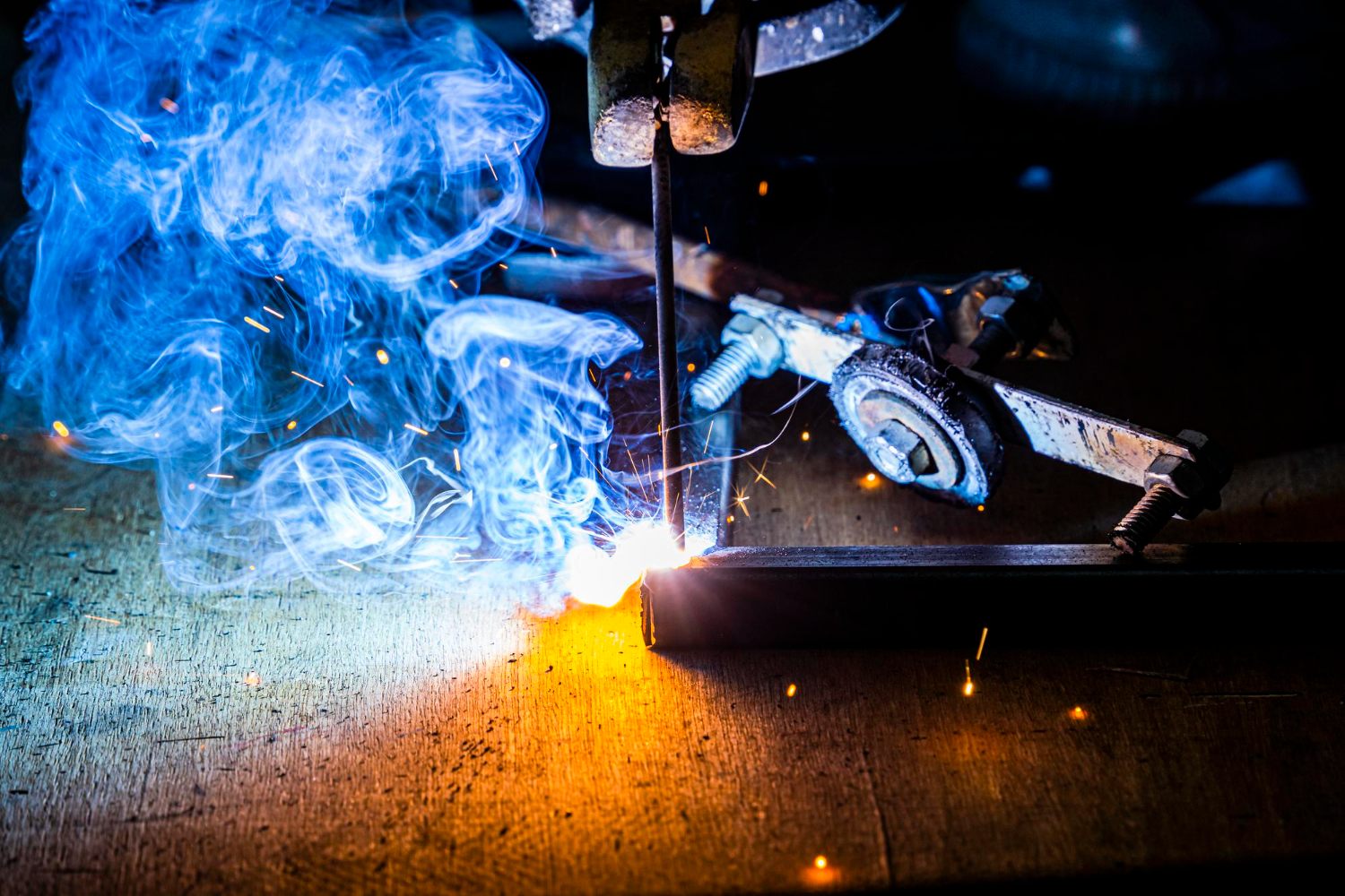 18781910 Close-up of welding repairs on metal with bright sparks and blue smoke rising from the work surface.