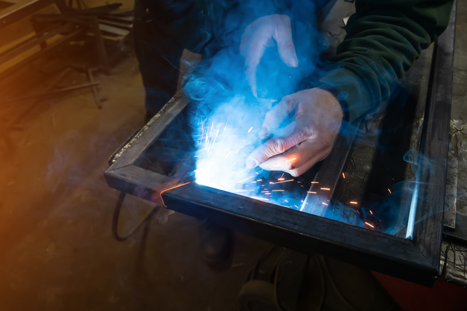 A person welding metal with sparks and smoke rising from the welding point.